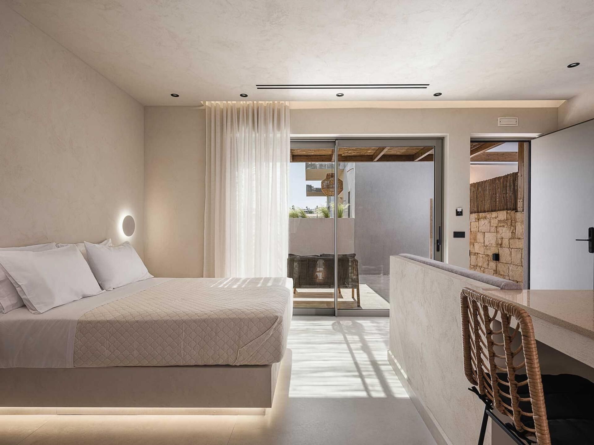 Un dormitorio moderno con cama, mesita de noche, silla y vista a un balcón exterior.