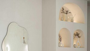 Une pièce moderne et minimaliste, dotée d’un grand miroir, d’un banc blanc et d’une étagère murale ornée de vases.