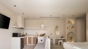 Une chambre moderne avec un grand lit, une petite kitchenette et une salle de bain équipée d’un miroir et d’étagères.
