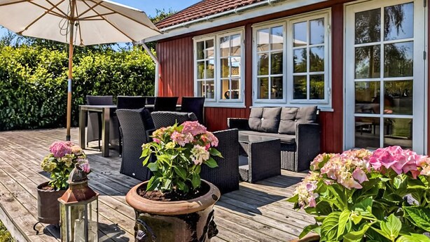 A wooden deck with outdoor furniture, including a table and chairs, and potted plants with flowers. - Gorgeous home in Væggerløse with WiFi (Væggerløse)