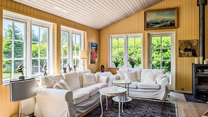 A cozy living room with a wooden ceiling, large windows, a white sofa set, a small round table, and a fireplace. - Gorgeous home in Væggerløse with WiFi (Væggerløse)