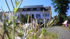 Ein zweigeschossiges Haus mit Solaranlage auf dem Dach, einer Schotterauffahrt und einem Garten mit verschiedenen Pflanzen und Blumen.