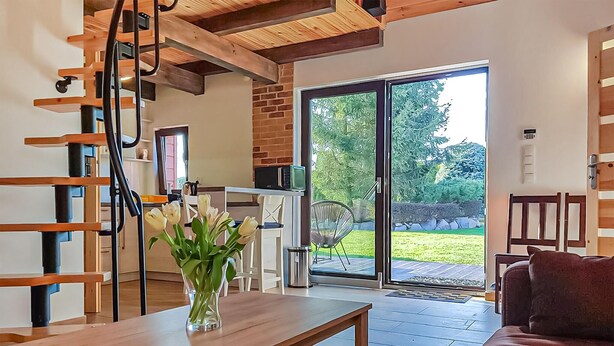A modern living room with a wooden table, a vase of flowers, a sofa, and a sliding glass door leading to a garden. - Nice home in Cieciorka with heated swimming pool (Cieciorka)