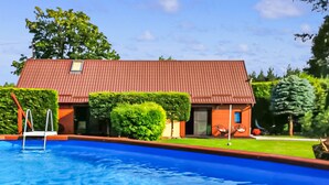 A swimming pool with a red-roofed building in the background, surrounded by greenery. - Nice home in Cieciorka with heated swimming pool (Cieciorka)