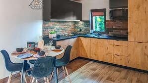 Eine moderne Küche mit einer Holzinsel, schwarzen Schränken und einer Ziegelrückwand. Es gibt einen Essbereich mit Tisch und Stühlen.