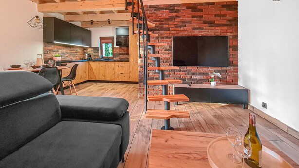 Ein modernes Wohnzimmer mit einer schwarzen Couch, einem Holztisch und einem an einer Ziegelwand montierten Fernseher.