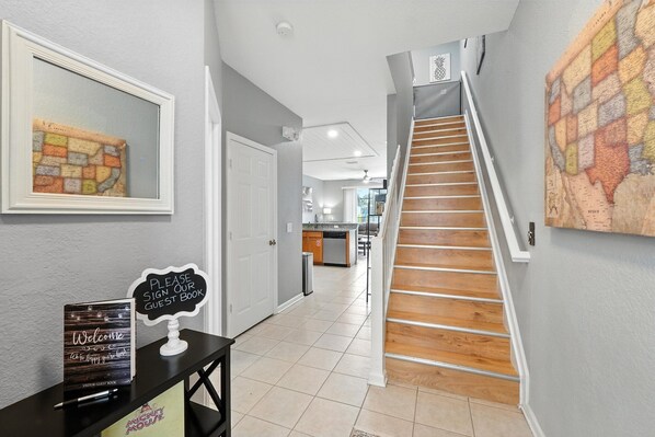 A hallway with a staircase, a guest book sign, and a map on the wall.