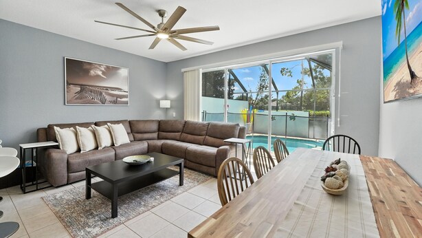 A living room with a sectional sofa, a dining table, and a ceiling fan. - Disney Escape - Private Pool & Full Resort Access (Kissimmee)