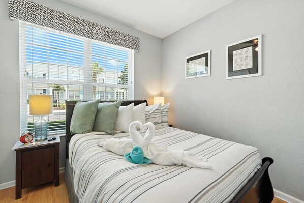 A neatly made bed with a striped bedspread, a nightstand with a lamp, and two framed pictures on the wall.