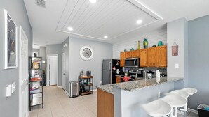 A modern kitchen with a central island, bar stools, wooden cabinets, and a microwave. - Disney Escape - Private Pool & Full Resort Access (Kissimmee)