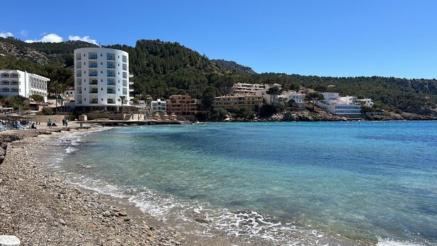 A coastal area with a rocky beach, clear blue waters, and buildings in the background. - Bright apartment with terrace & sea view (IB)