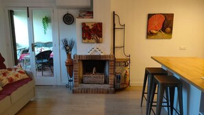 A cozy living room with a fireplace, a dining area with a table and chairs, and a kitchen area with a bar stool. - Bright apartment with terrace & sea view (IB)