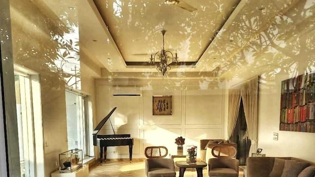 Un vaste salon doté d’un parquet en bois disposé en point de Hongrie, d’un piano à queue, d’un canapé et d’un lustre.