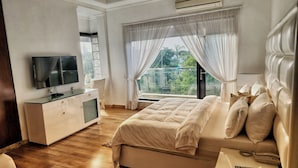 Une chambre à coucher avec un lit, une télévision, une commode et une fenêtre avec des rideaux.