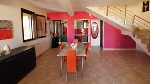 A dining area with a table and chairs, a staircase, and a kitchen area with red cabinets.