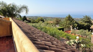 A rooftop terrace with a view of the sea and surrounding greenery.