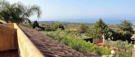 A rooftop terrace with a view of the sea and surrounding greenery.