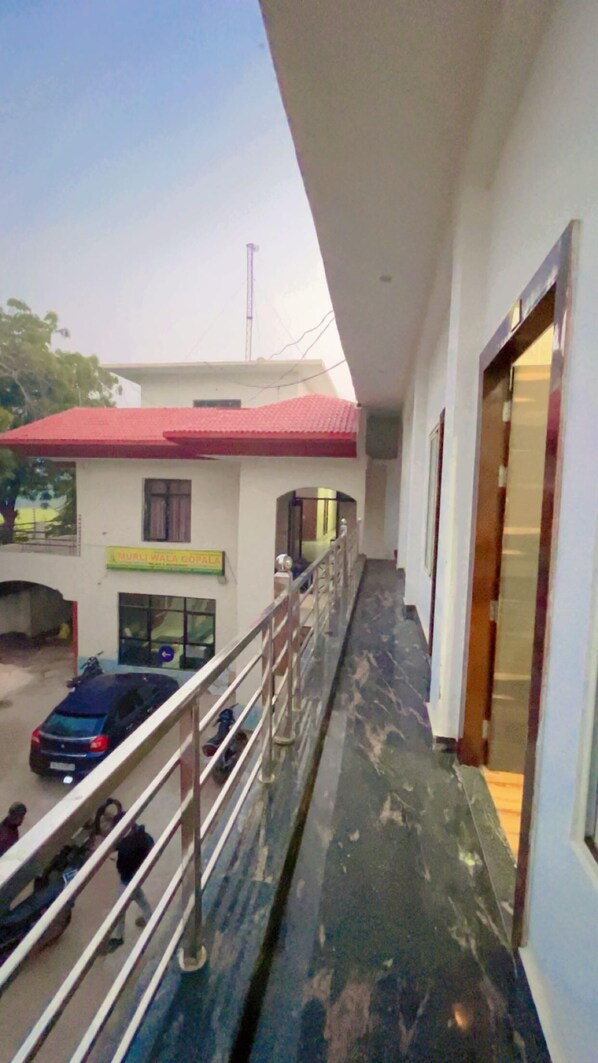 A corridor with a metal railing, a building with a red roof, and a sign that reads "MURLI WALA GOPAL".