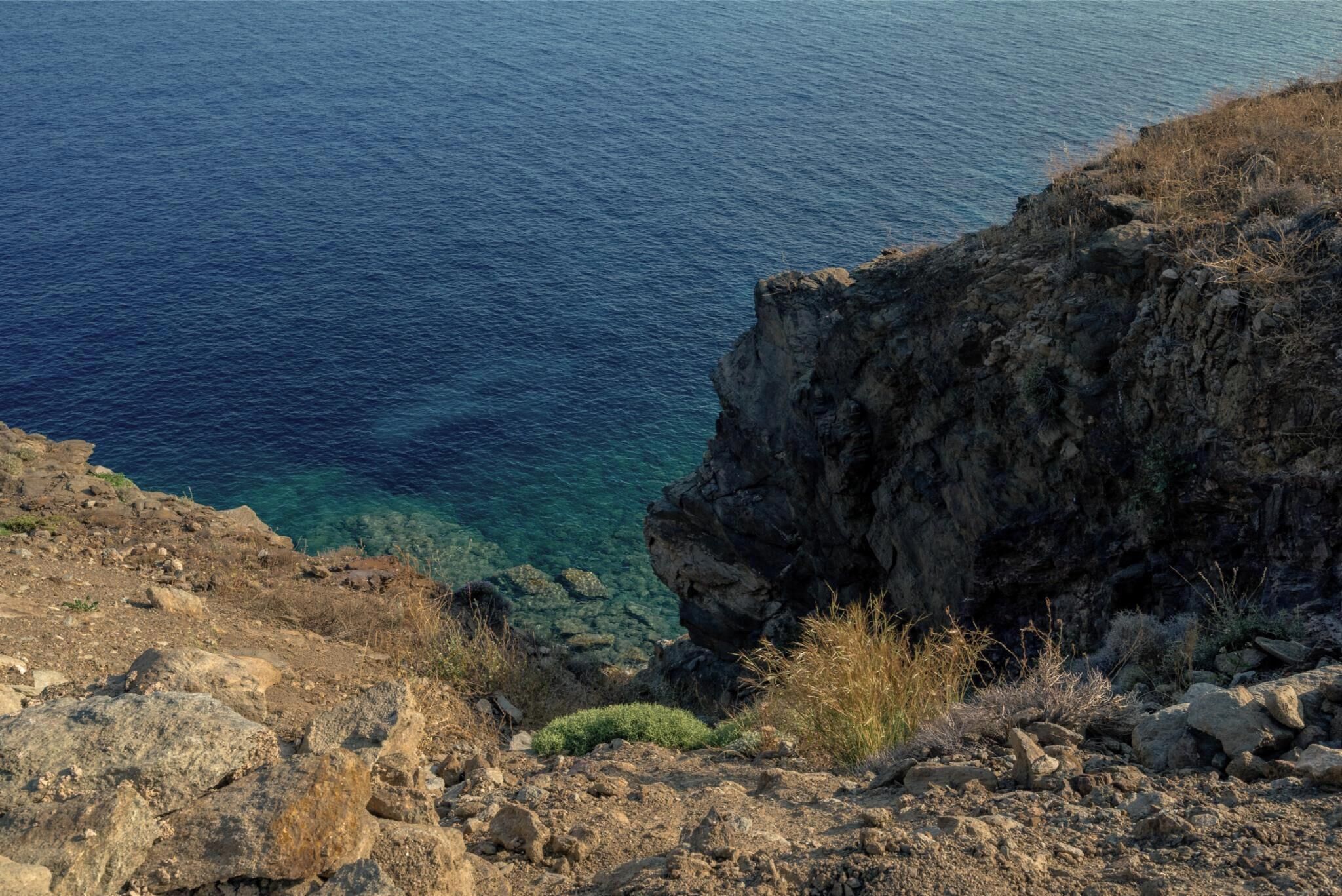Eine felsige Küstenlinie mit klarem, blauem Meer und spärlicher Vegetation.