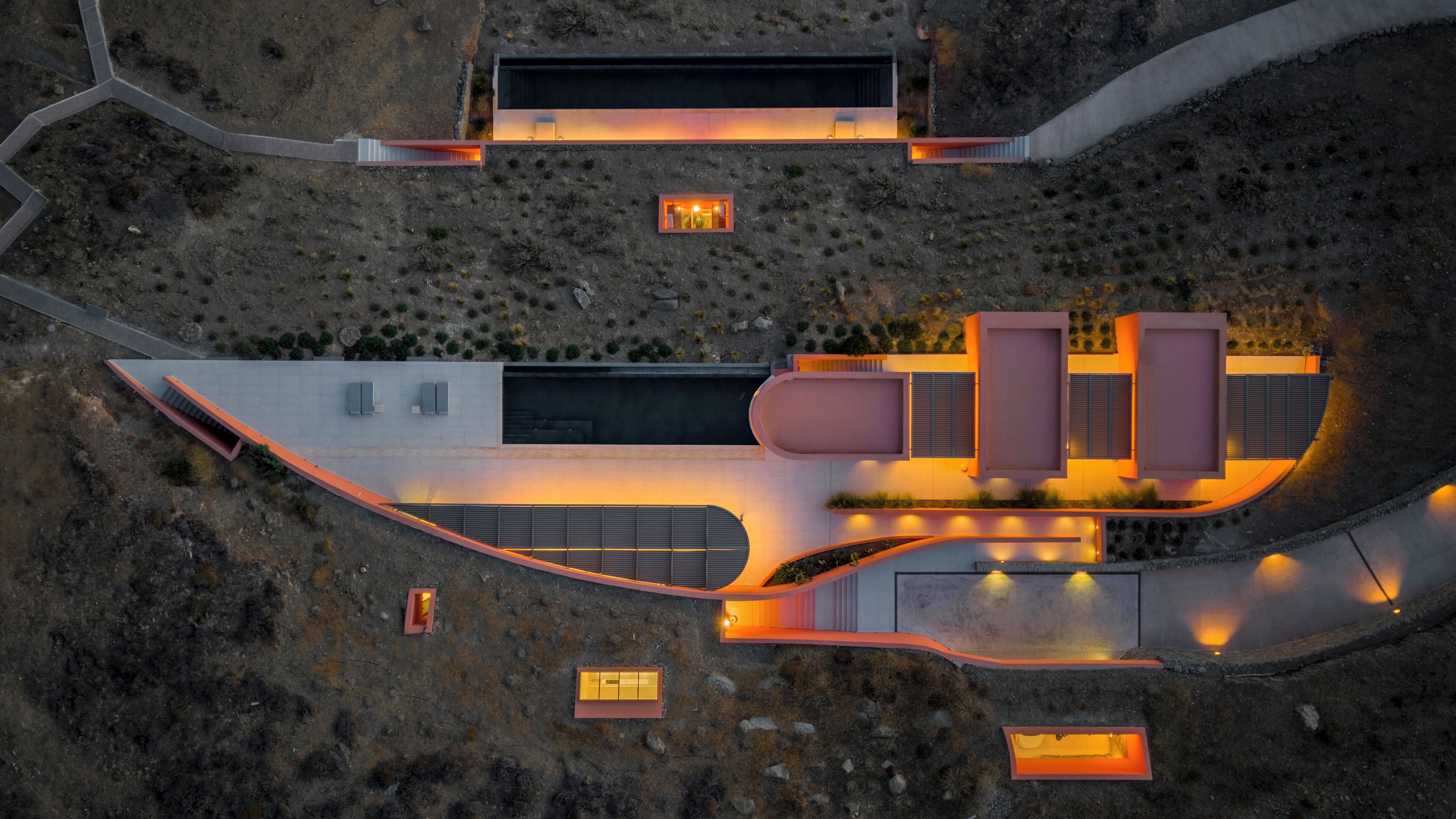 An aerial view of a modern building with a swimming pool, outdoor seating areas, and a landscaped garden.