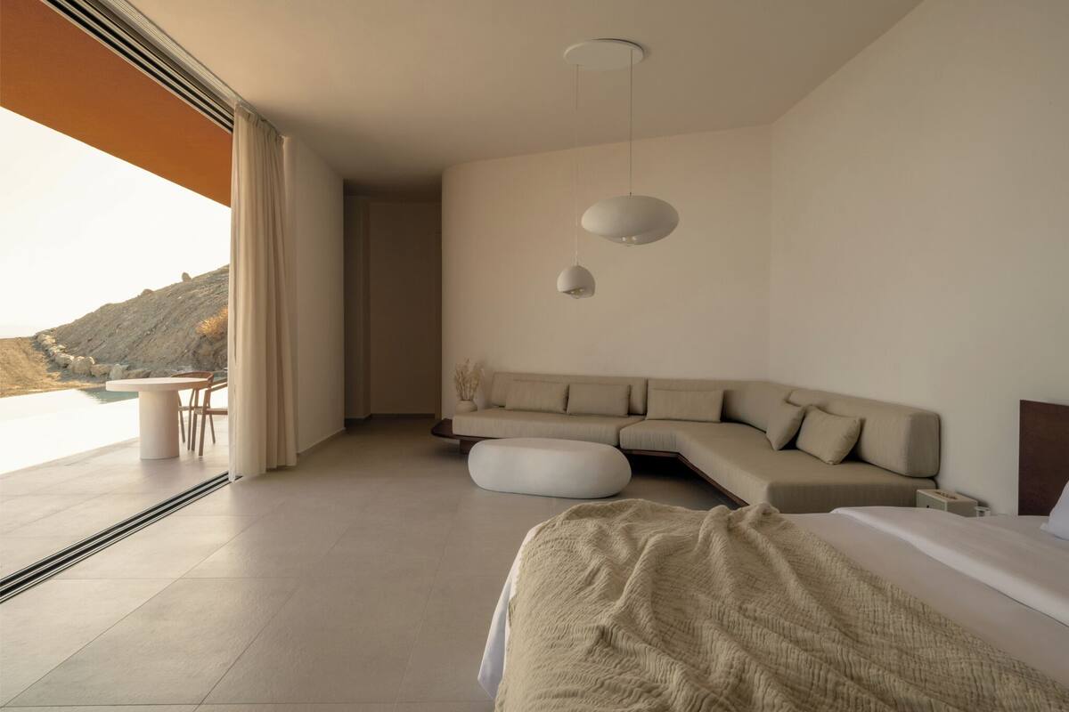 A modern bedroom with a large bed, a sofa, and a dining area with a table and chairs.