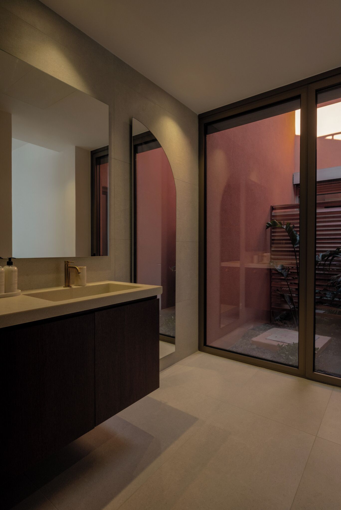 A modern bathroom with a large mirror, two sinks, and a sliding glass door leading to an outdoor area.