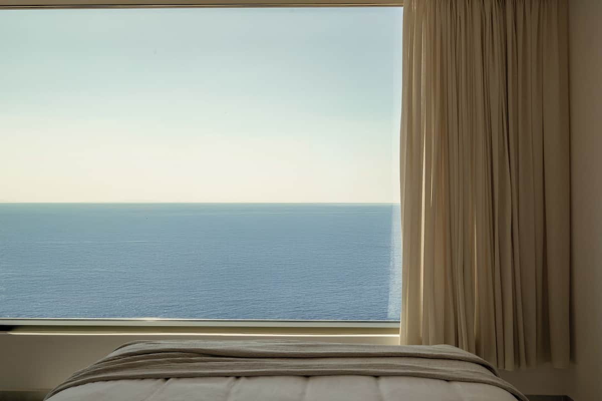 A bed with a view of the sea through a window.