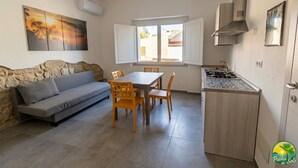 Un espacio habitable compacto con sofá, mesa de comedor, sillas, zona de cocina con estufa y ventana con persianas abiertas.