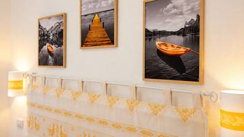 A hotel room with a bed, a curtain with a golden pattern, and three framed pictures on the wall.
