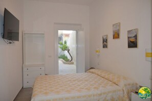 A bedroom with a bed, a TV, a wardrobe, and a door leading to a balcony with a potted plant.