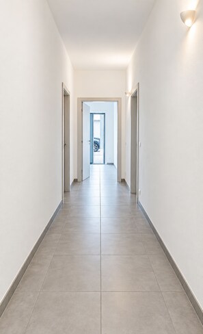 A corridor with a tiled floor and white walls, leading to a door at the end. - Private RED Apartment at Palma de Sols – No Shared Living Spaces (Sant'antioco)