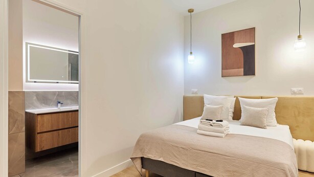 Une chambre à coucher moderne, comprenant un lit, des tables de chevet, une commode, un grand miroir et un luminaire fixé au mur.