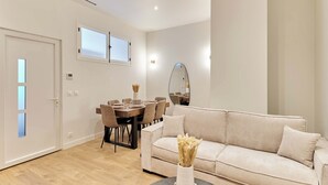 Un salon moderne avec un canapé beige, une table à manger avec des chaises et une petite table ronde sur laquelle est posé un vase.