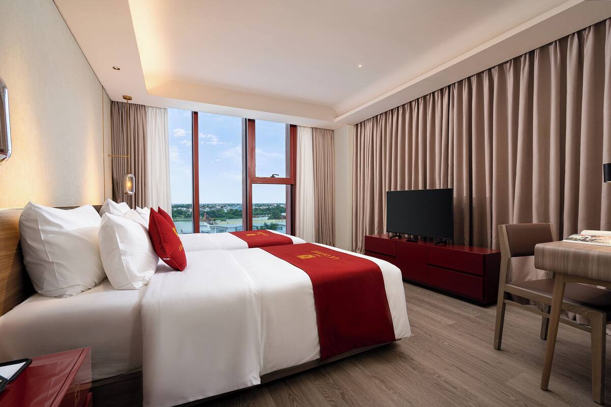 A hotel room with a large bed, a TV, a desk, and a view of the sea.