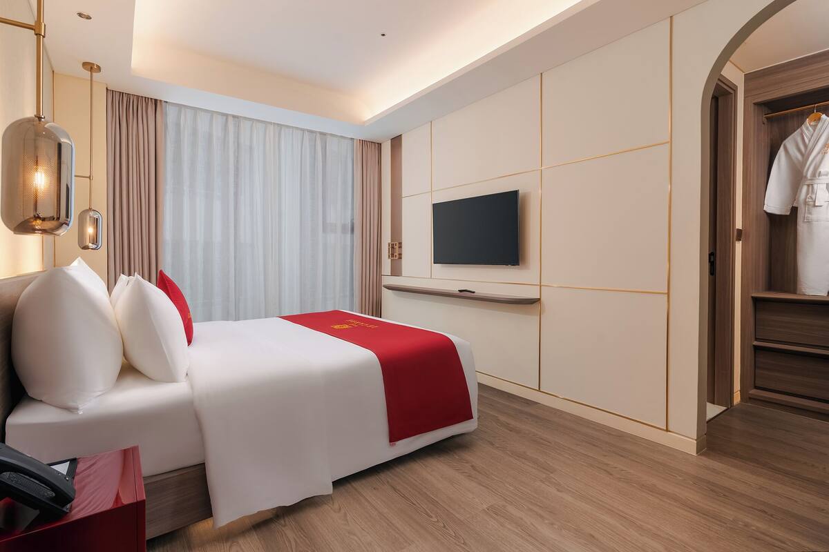 A hotel room with a bed, a TV, a wardrobe, and a red accent on the bedspread.