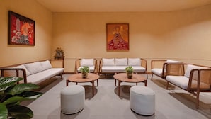 A modern lounge with a sofa set, two round tables with plants, and artwork on the walls. - Le Carré Hue (Hue)