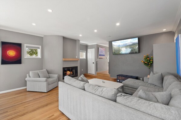Ein modernes Wohnzimmer mit Kamin, grauen Sofas, einem Couchtisch und Kunstwerken an den Wänden.