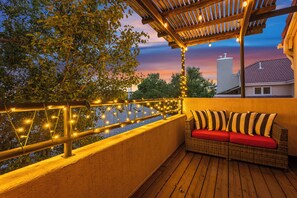 Ein Balkon mit Rattan-Sofa, Lichterkette und Blick auf ein Gebäude im Hintergrund.