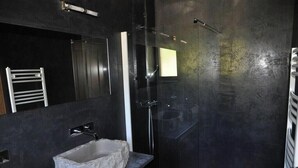 A modern bathroom with a dark wall, a stone sink, a mirror, and a glass-enclosed shower. - Gîte de Jassenove (Jassenove-du-Larzac)
