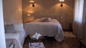 A bedroom with a bed, two wall-mounted lamps, a small table with a tissue, and a chair. - Gîte de Jassenove (Jassenove-du-Larzac)