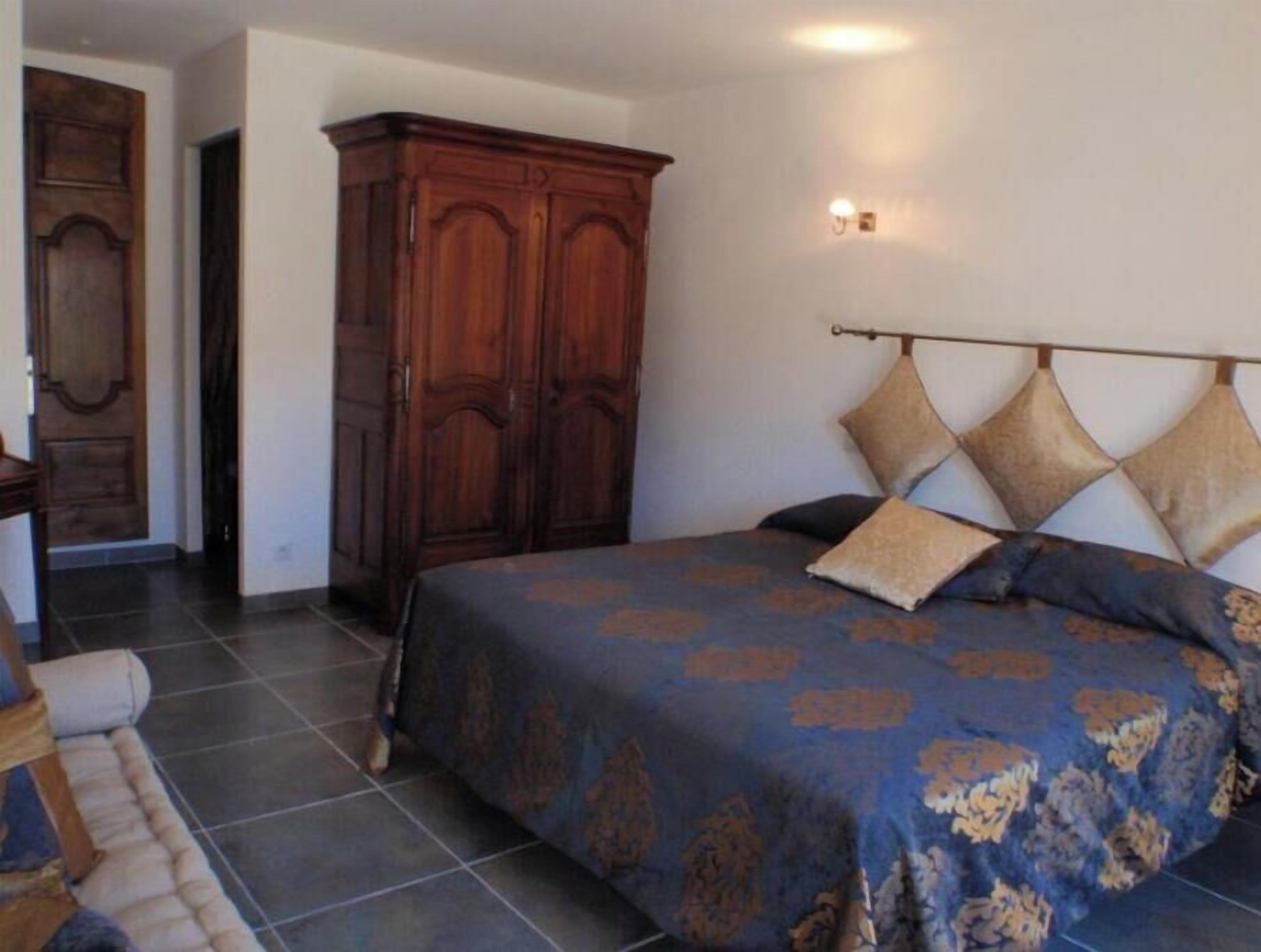 A bedroom with a large bed, a wooden wardrobe, and a nightstand.