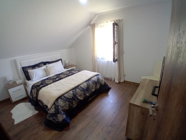 Un dormitorio con una cama, una mesita de noche, un escritorio y una ventana con cortinas.