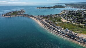 Vista aérea de uma cidade costeira com um porto de iates, praia de areia e edifícios residenciais ao longo da costa.