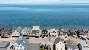 Uma área residencial costeira com casas ao longo da orla, vista clara do oceano e uma estrada em primeiro plano.