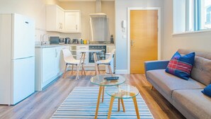 A compact living space with a kitchenette, a dining area with chairs, a sofa with a plaid cushion, and a glass coffee table. - Chic Loft Apartment in Kelham Island, Sheffield (South Yorkshire)