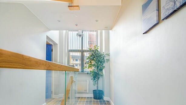 A modern hallway with a glass railing, a patterned floor, and a potted plant. - Chic Loft Apartment in Kelham Island, Sheffield (South Yorkshire)