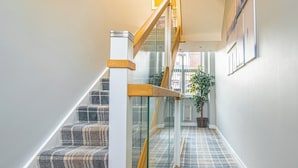 A staircase with a wooden handrail and glass balustrade, leading to a landing with a potted plant. - Chic Loft Apartment in Kelham Island, Sheffield (South Yorkshire)