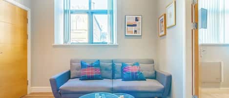 A cozy living room with a grey sofa, a glass coffee table, and a striped rug.