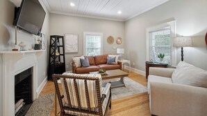 A living room with a fireplace, a brown leather sofa, a striped armchair, and a beige armchair. - Bluebird Cottage in heart of Hickory, NC (Hickory)