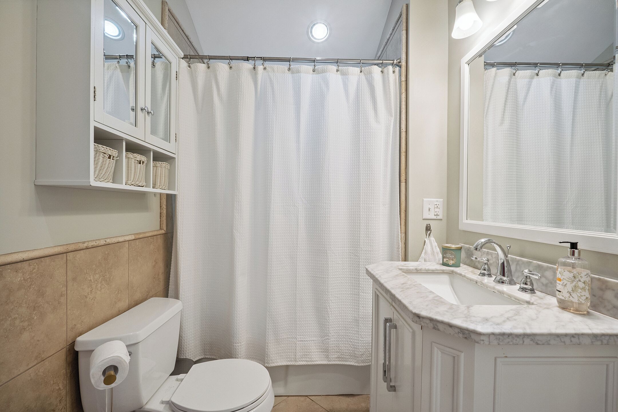 Un baño con inodoro, cortina de ducha, lavamanos con espejo y armarios de almacenamiento.